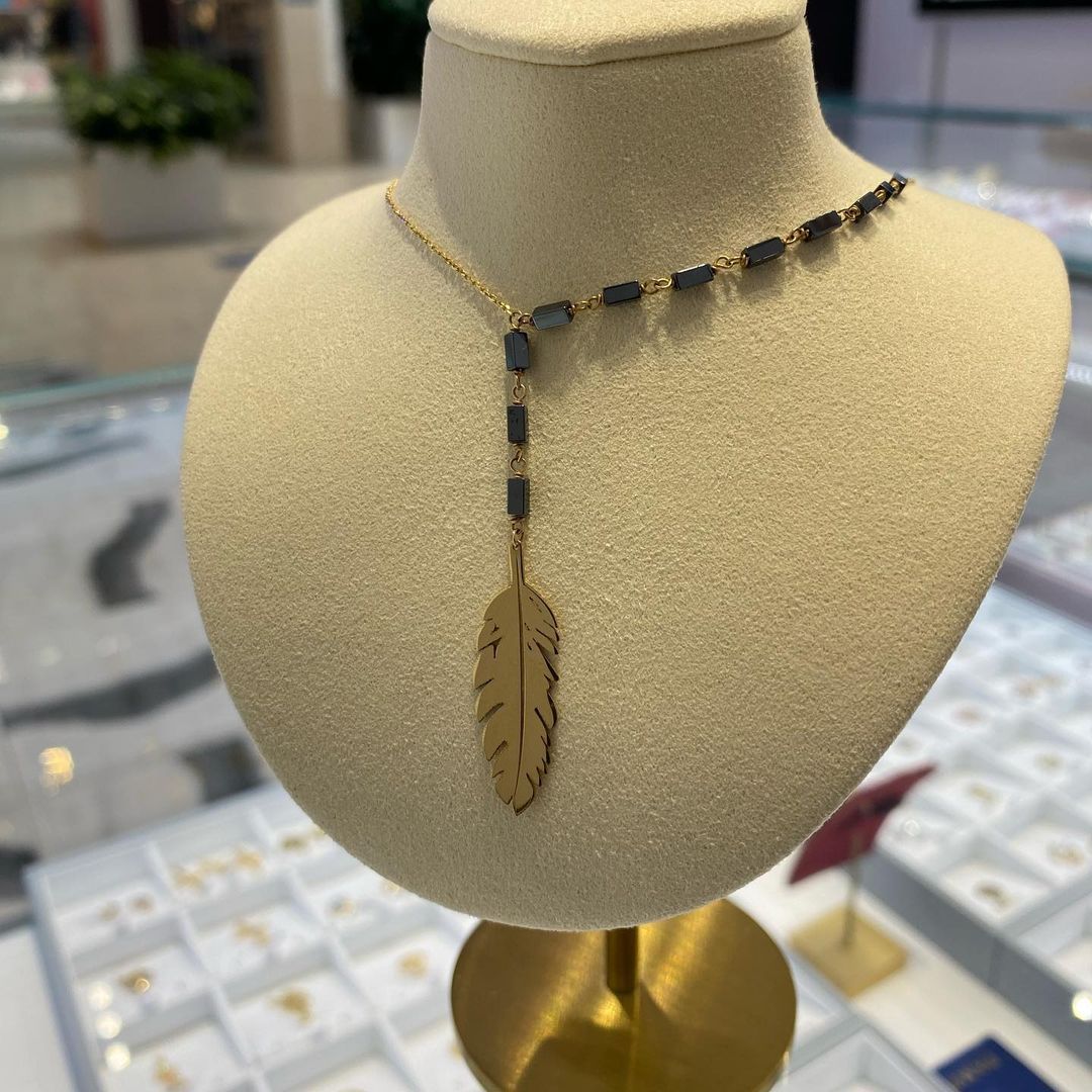 A necklace with a feather pendant is on a mannequin.