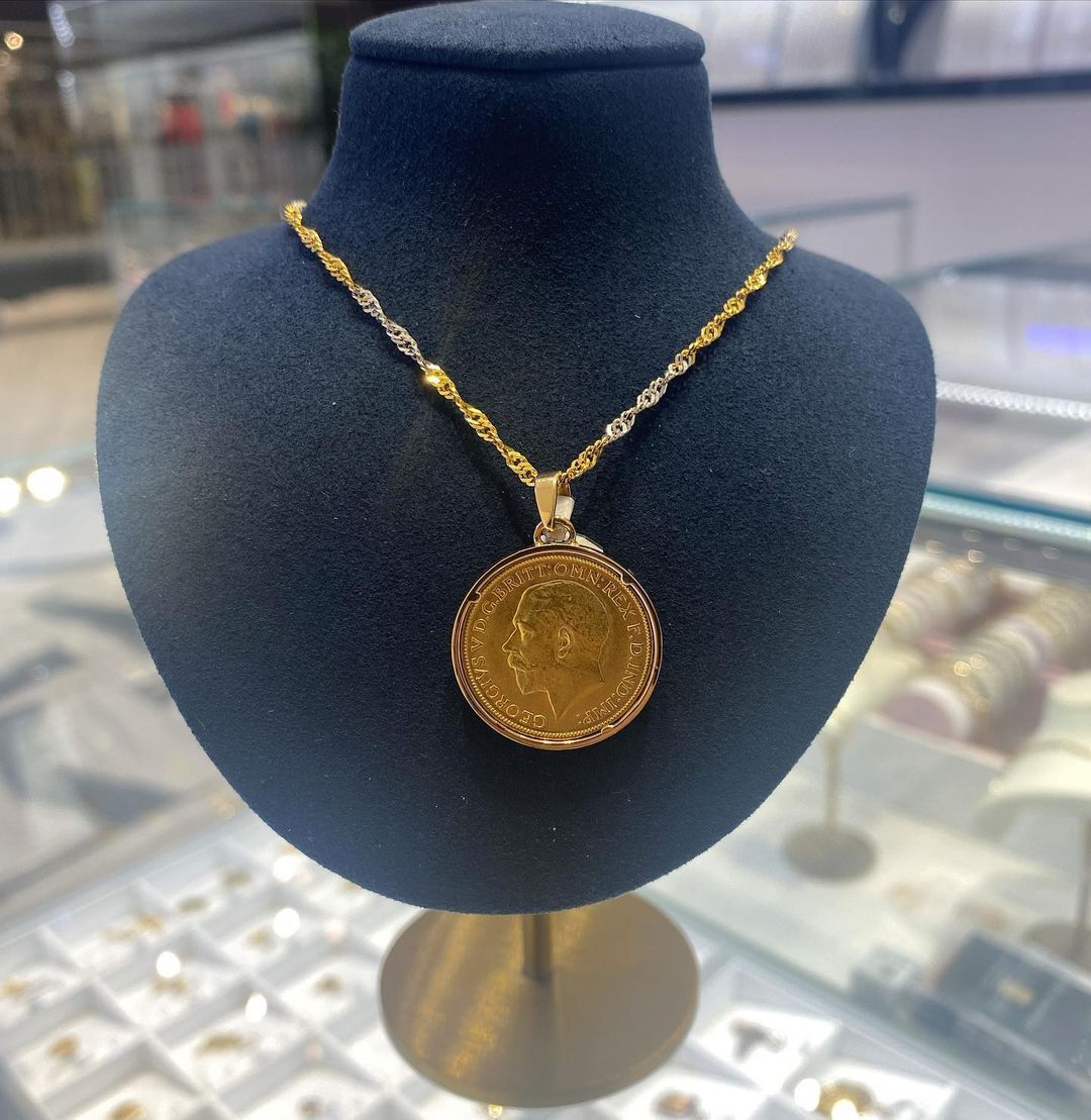 A gold necklace with a coin pendant on a mannequin
