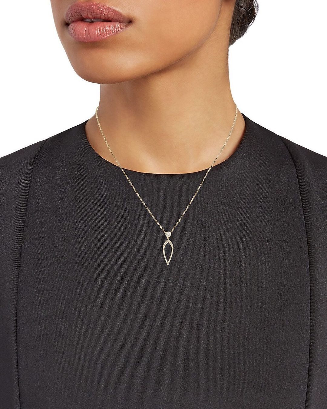 A woman is wearing a necklace with a leaf shaped pendant.