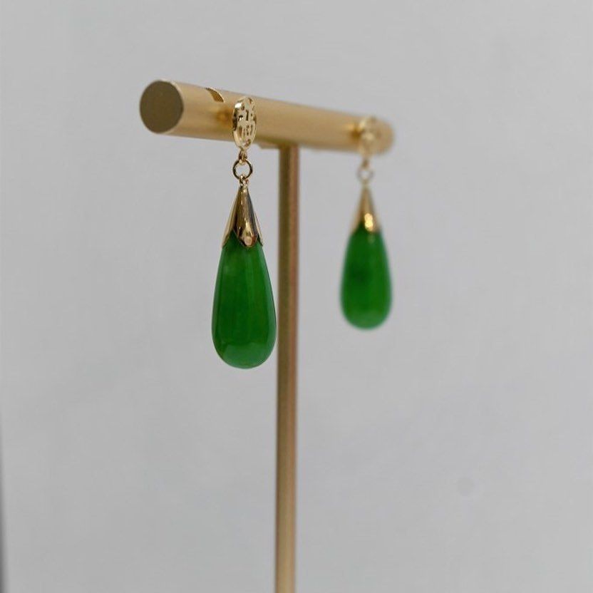 A pair of green earrings are sitting on a gold stand.