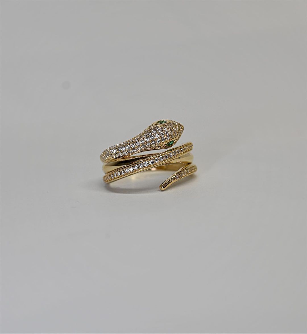 A gold ring with a snake on it is on a white surface.