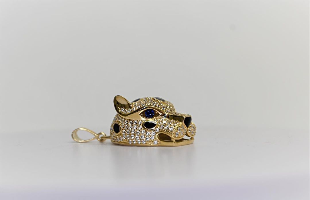 A gold pendant in the shape of a cheetah 's head with diamonds and sapphires.