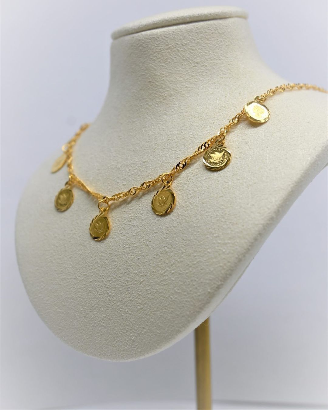 A gold necklace is displayed on a mannequin
