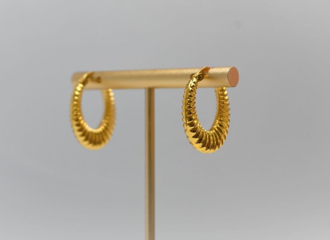 A pair of gold hoop earrings are sitting on a gold stand.