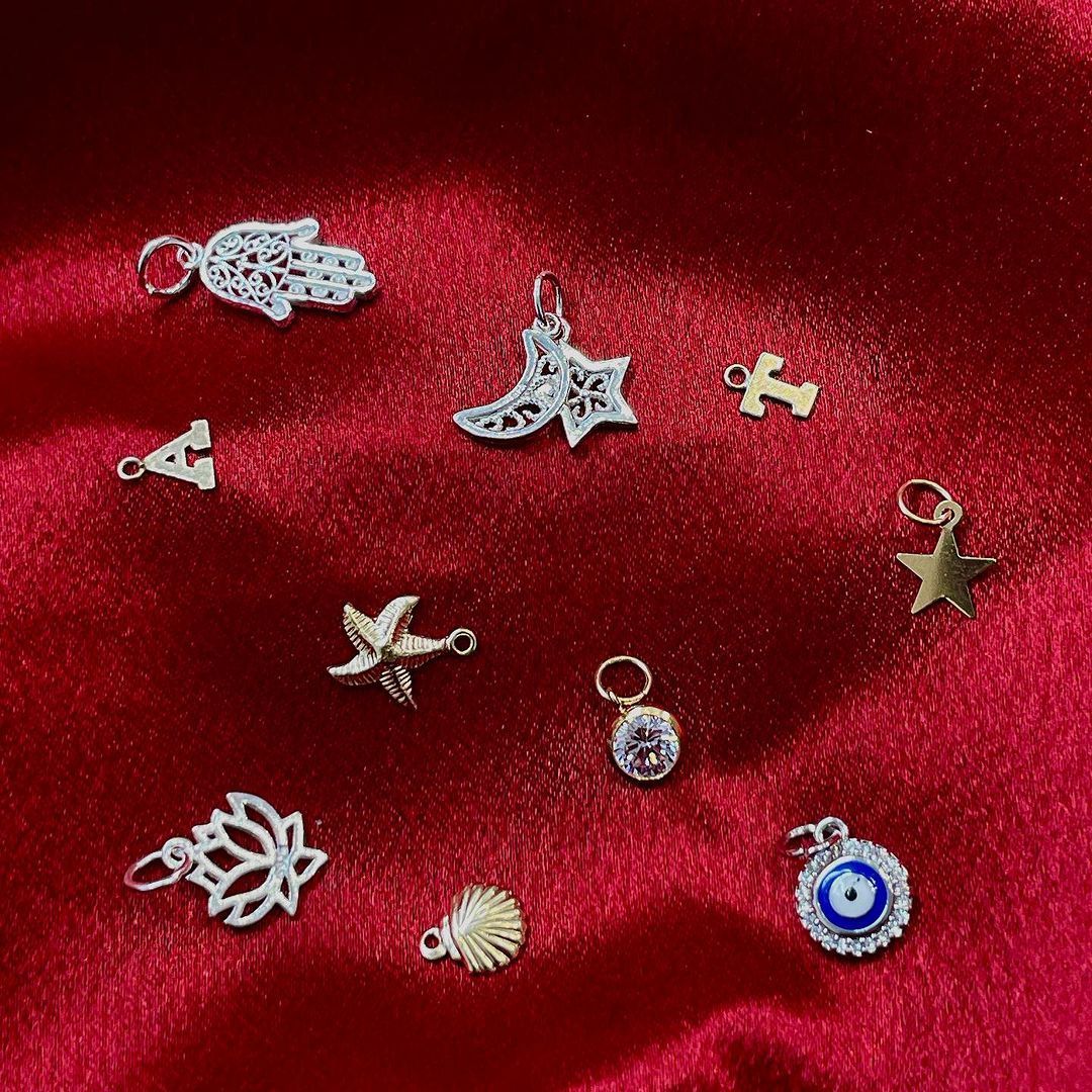 A variety of silver charms are sitting on a red cloth.