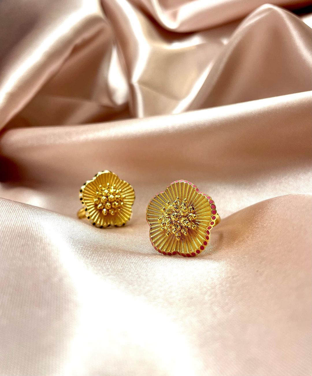 A pair of gold cufflinks are sitting on a pink cloth.