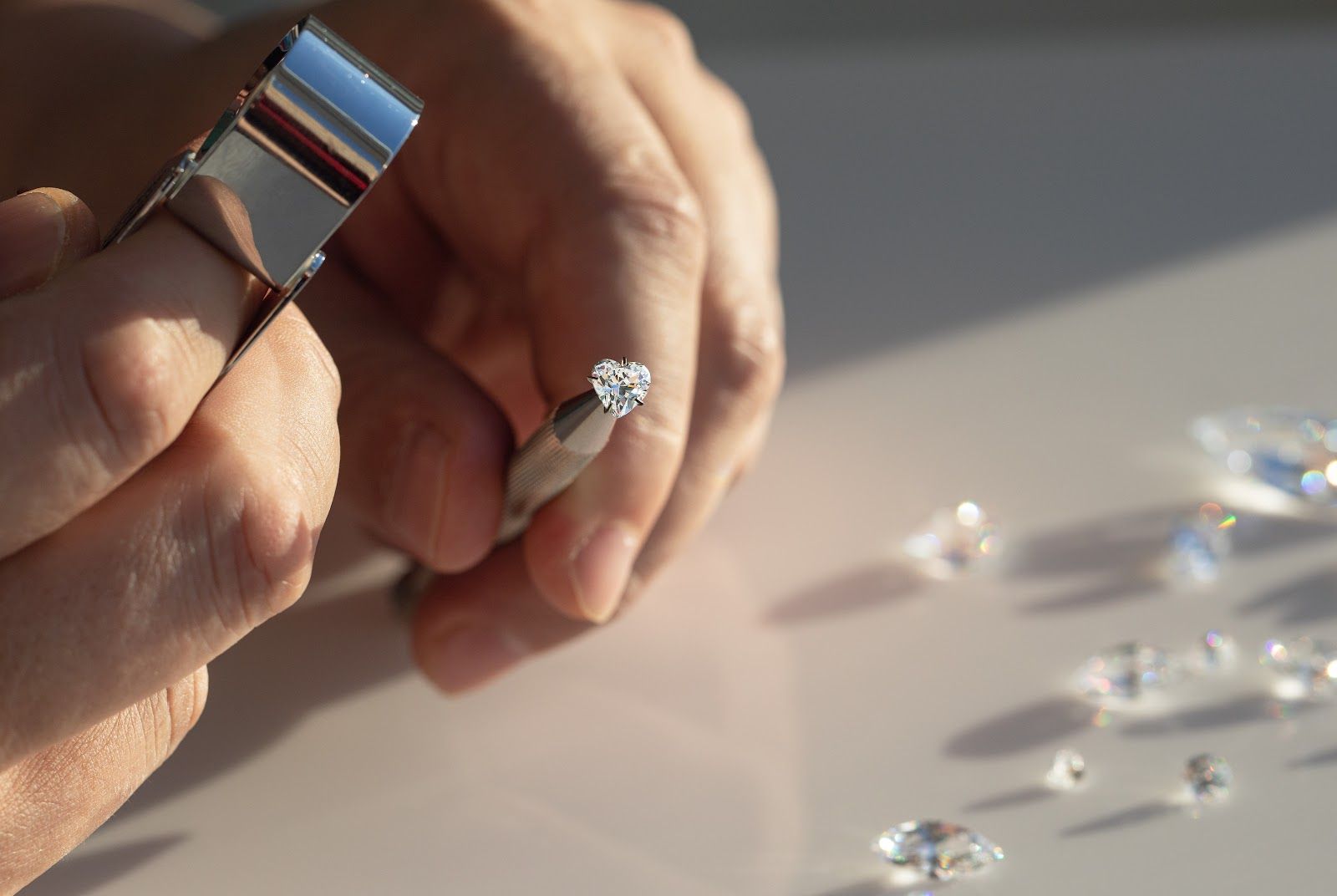 Hands using jeweler’s loupe and tool to inspect a diamond ring on a white table