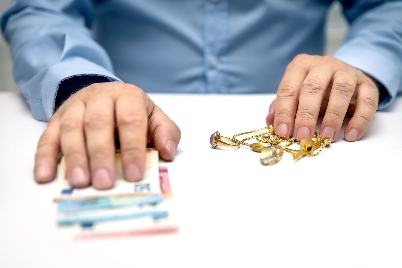 Hands with cash and gold jewelry on a white table, suggesting financial comparison or trade