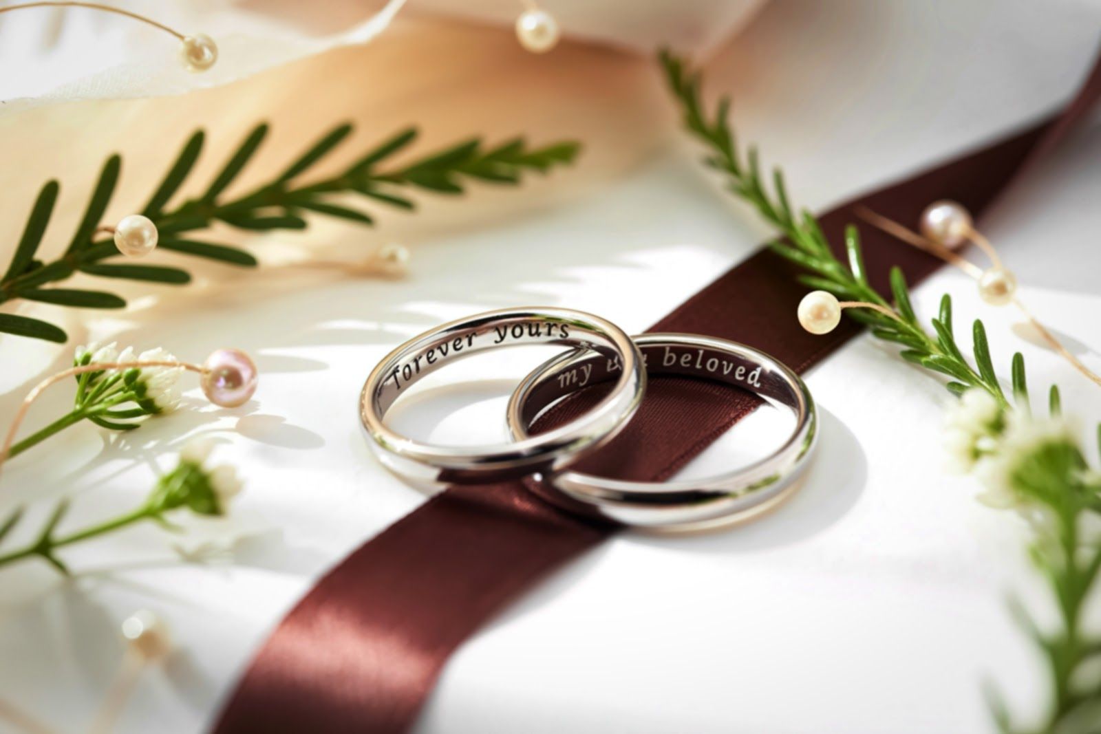 Two silver wedding rings on a burgundy ribbon with greenery and pearls