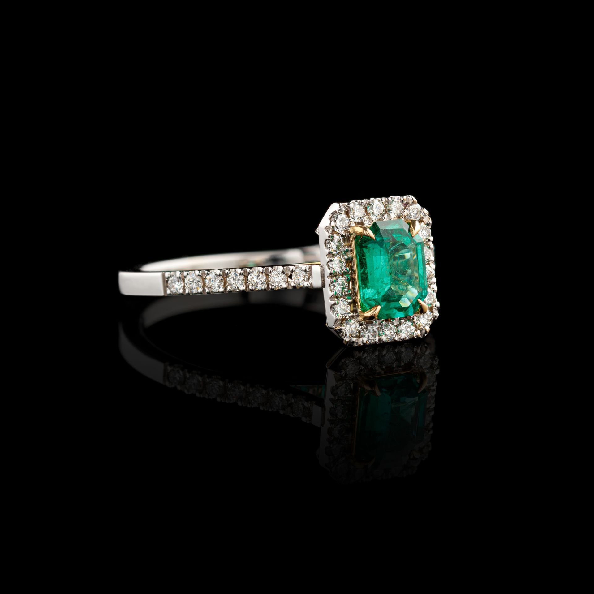 A ring with an emerald and diamonds on a black background.