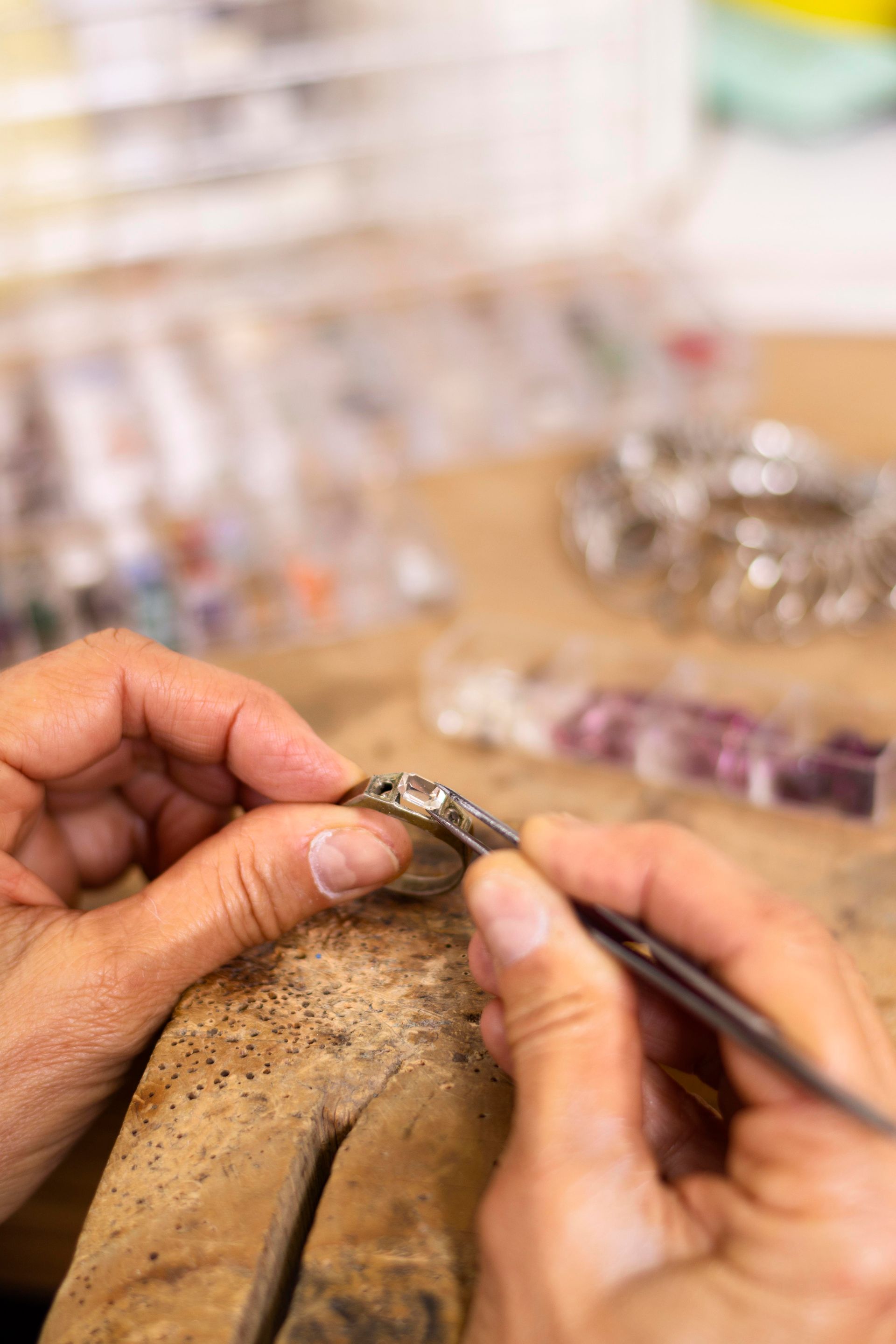 A person is working on a piece of jewelry on a wooden table.
