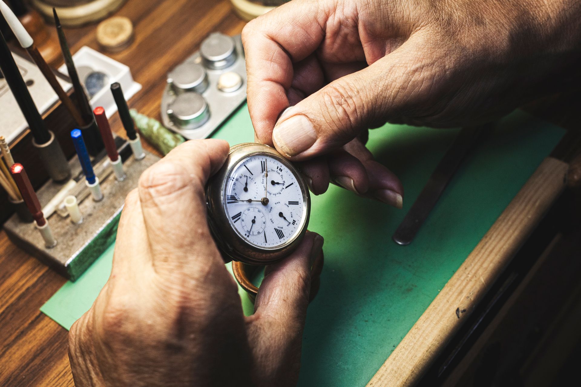 A man is fixing a watch on a green table.