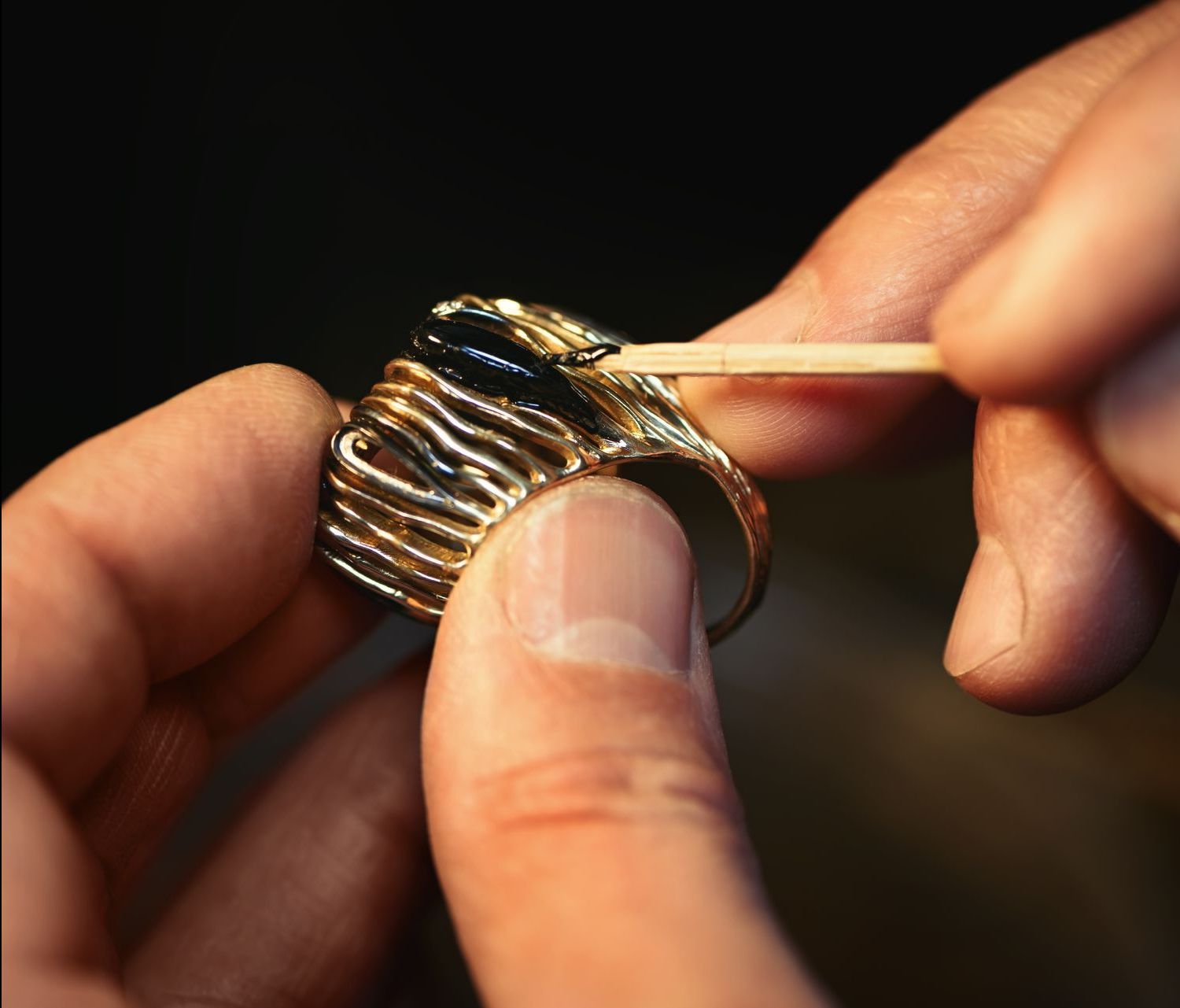 A person is cleaning a gold ring with a toothpick