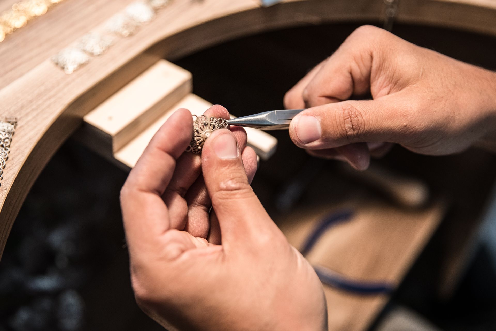 A person is working on a piece of jewelry with a pair of pliers.