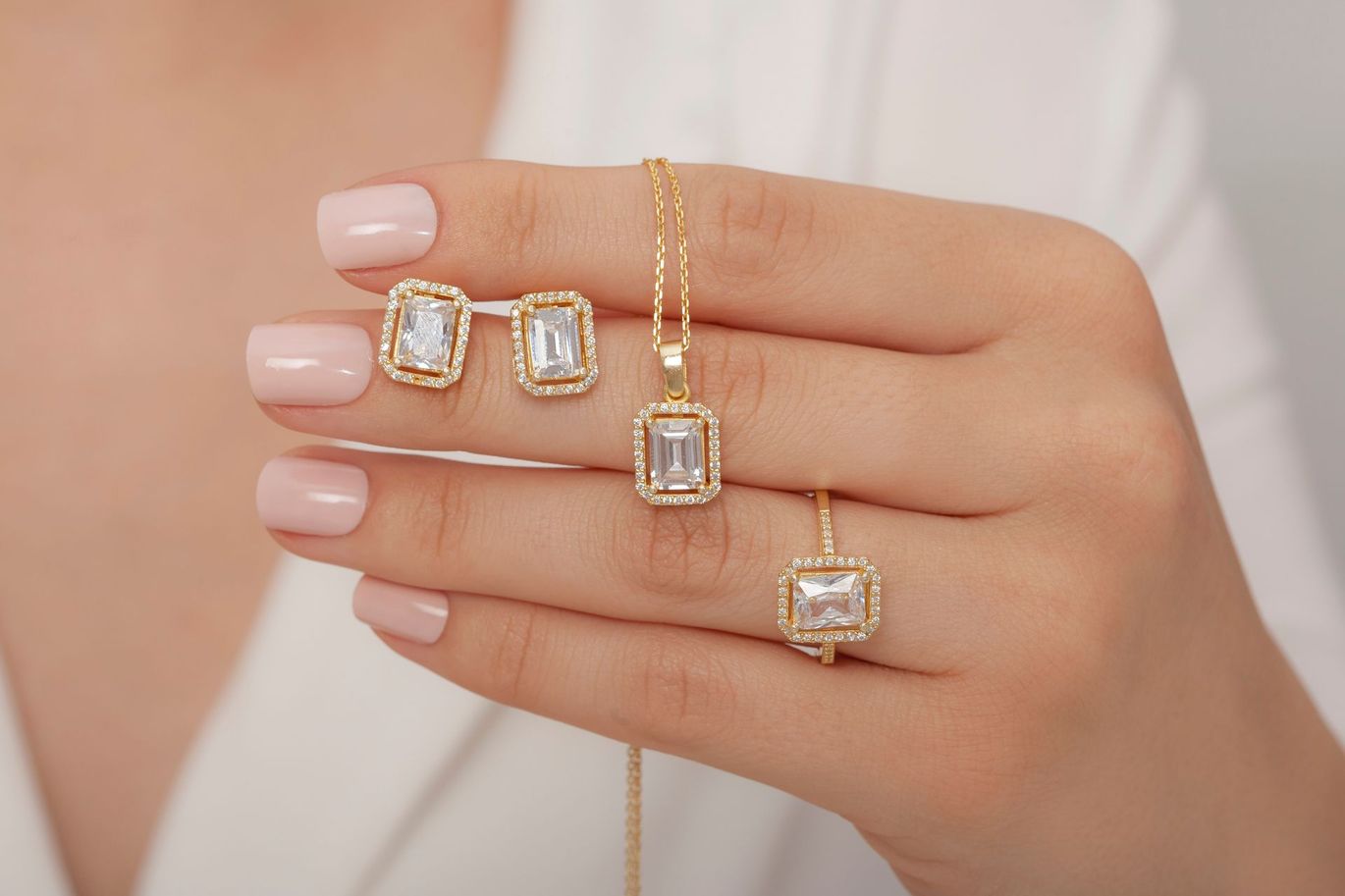 Hand with pink nails wearing gold ring bracelets with clear square stones