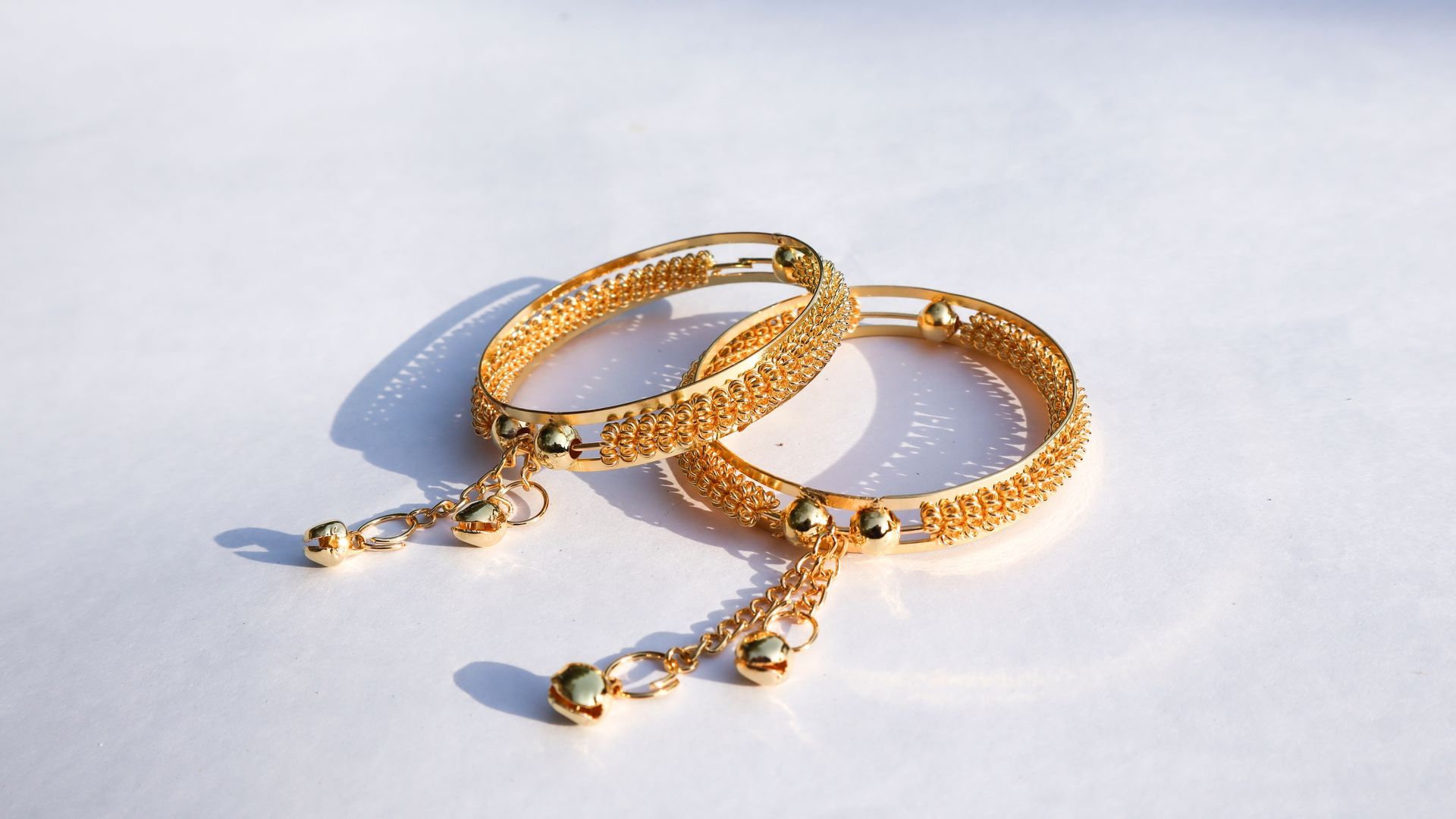 A pair of gold bracelets on a white surface