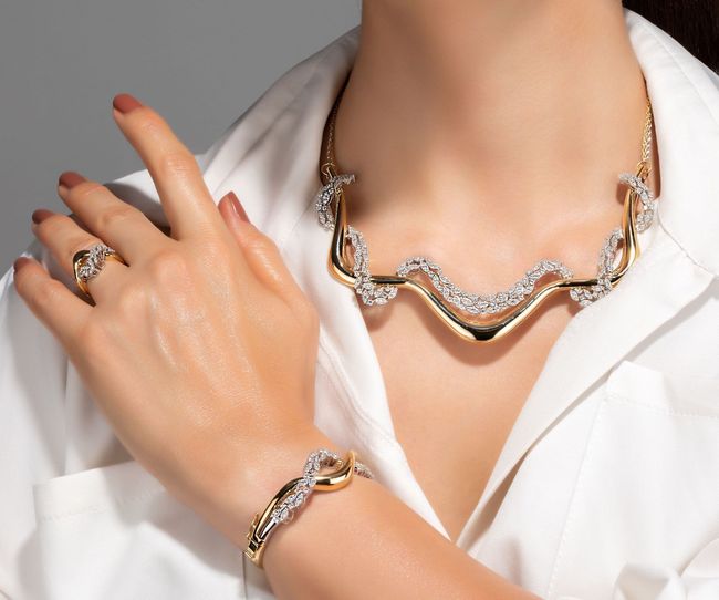 Close-up of a hand wearing gold and diamond jewelry over a white shirt collar.