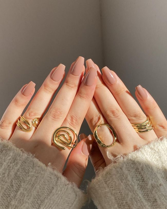 Hands with gold rings held together in soft beige sleeves against a neutral background
