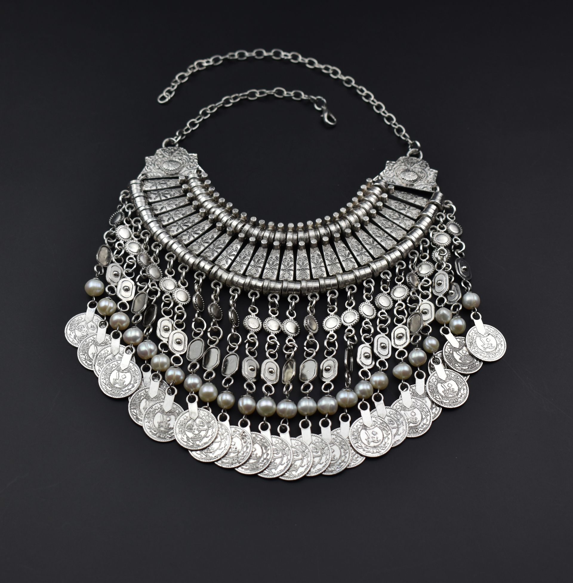 A silver necklace with pearls and coins on a black background