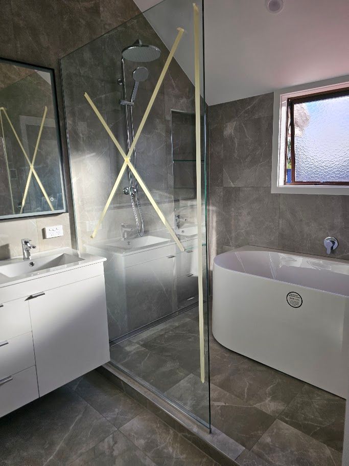 Glass-enclosed shower with dark tile under renovation