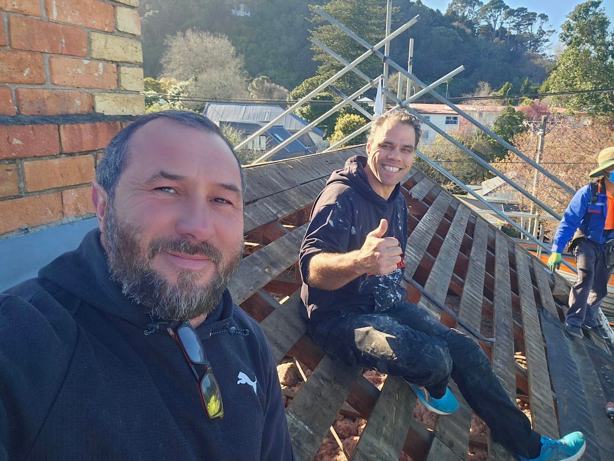 Two people posing near roof scaffolding at a brick building