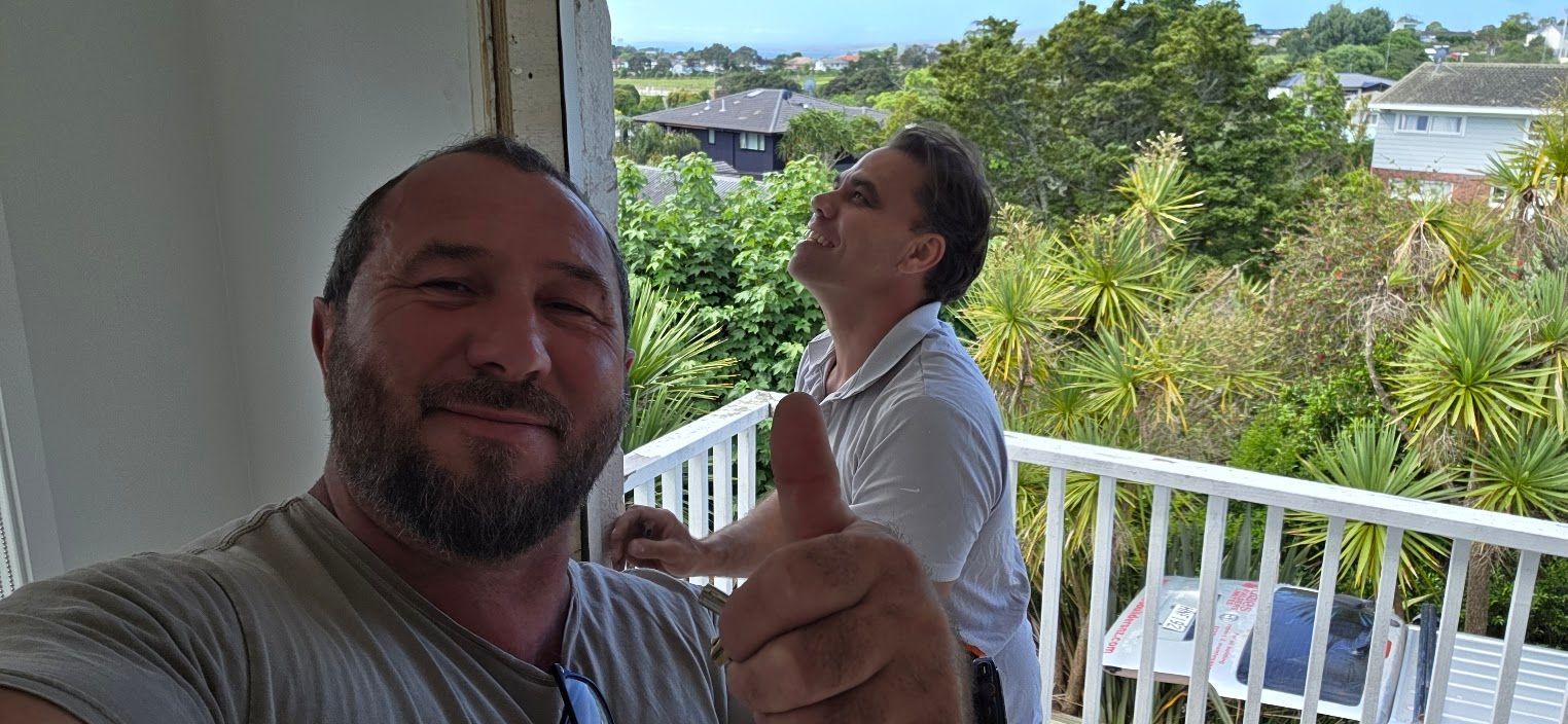 Two men on a balcony overlooking a coastal neighborhood
