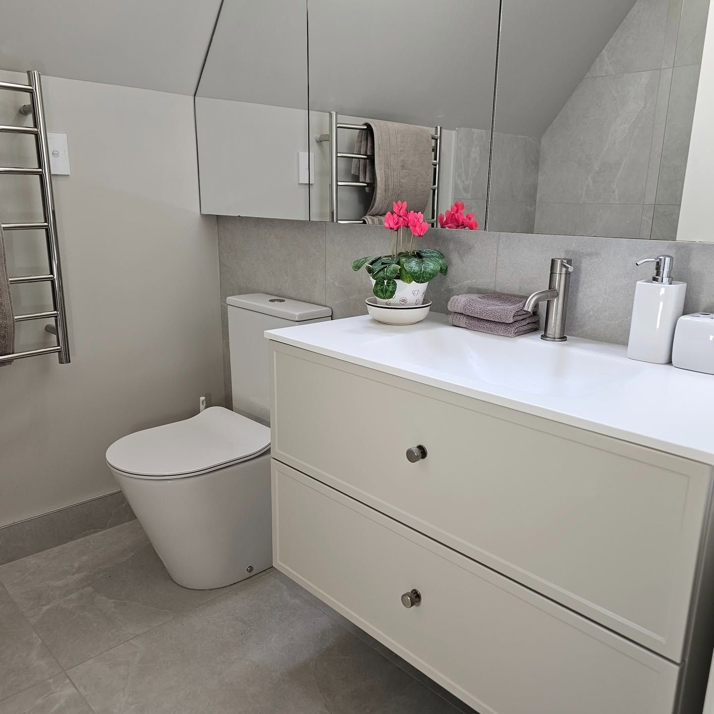 Bathroom vanity with marble-look tile, chrome towel rail, and pink flowers