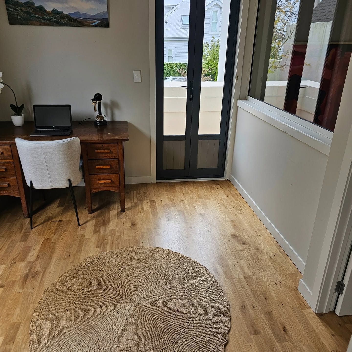 Open balcony door beside a desk with a laptop and framed artwork