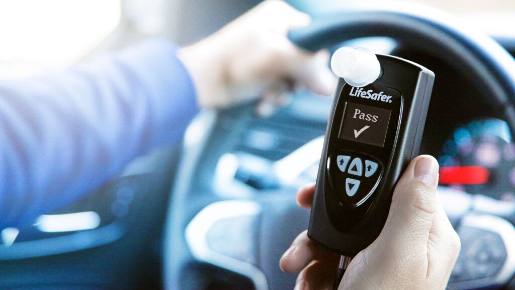 Hands holding a black breathalyzer in a car, testing the driver