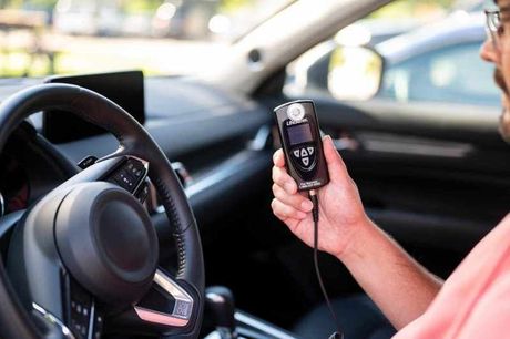 Hand holding a car key fob beside the steering wheel inside a parked car