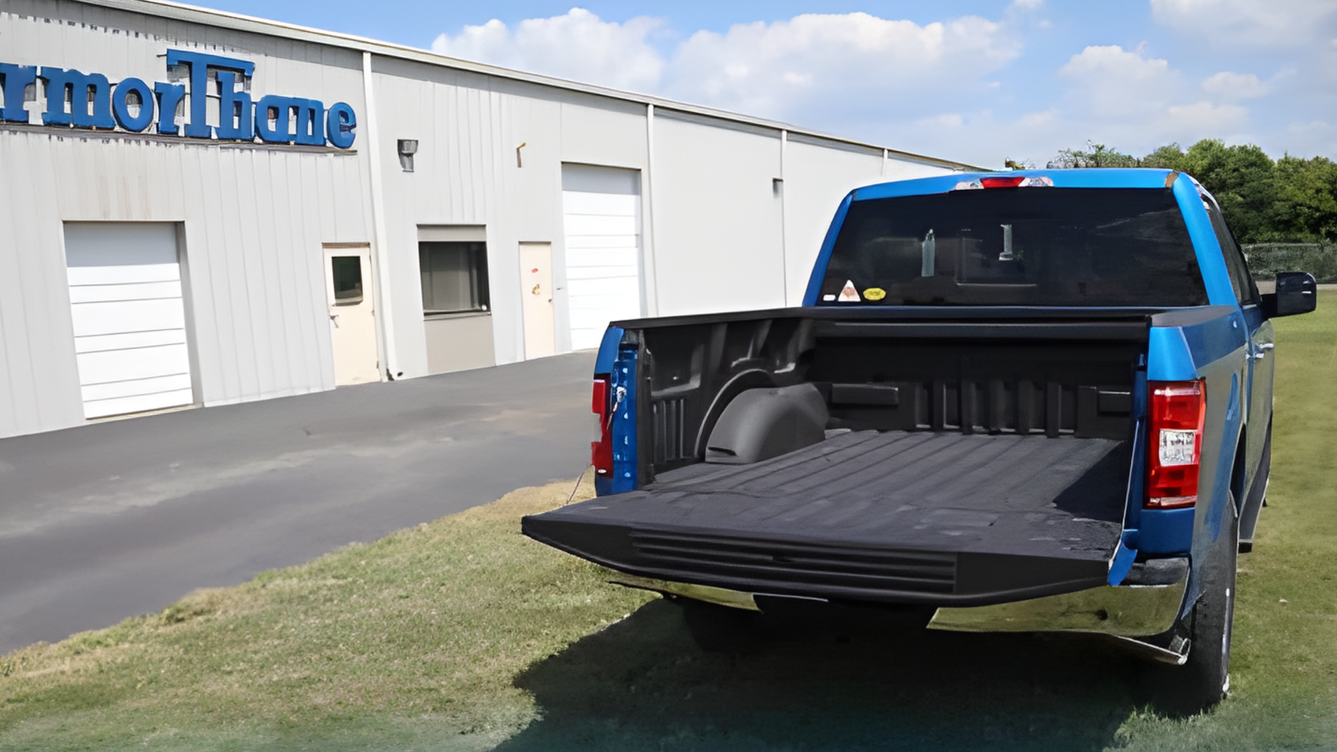 Blue pickup truck with open tailgate parked outside a white commercial building
