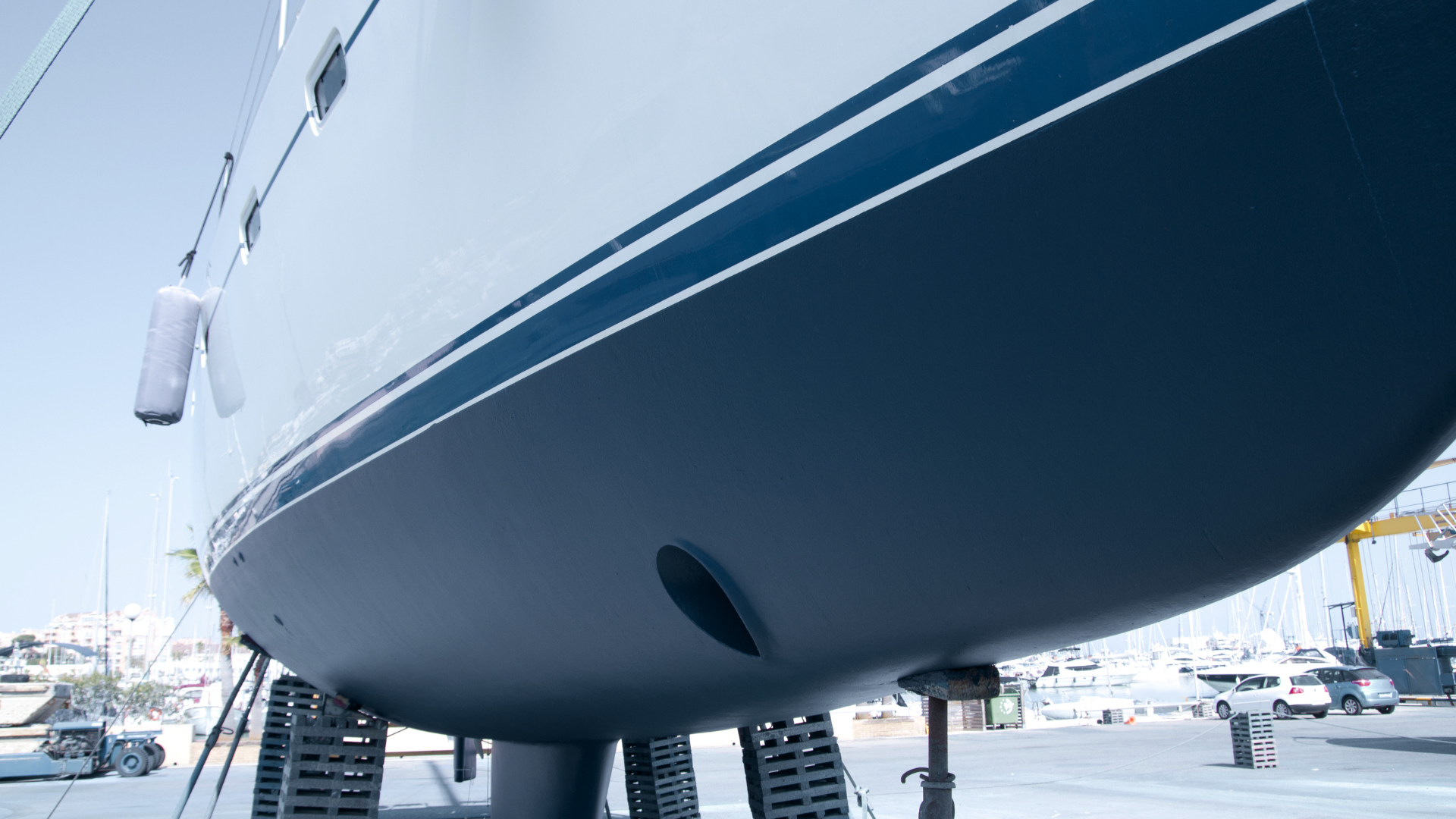 Low-angle view of a white and navy sailboat hull on supports in a marina