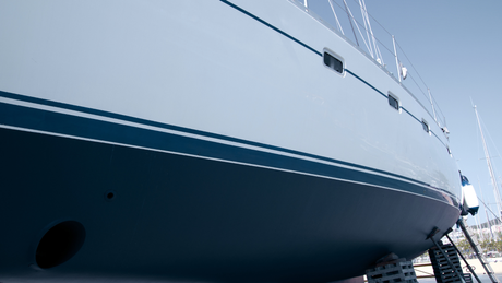 Close-up of a white yacht hull docked at a marina, with dark blue waterline and metal railing above.