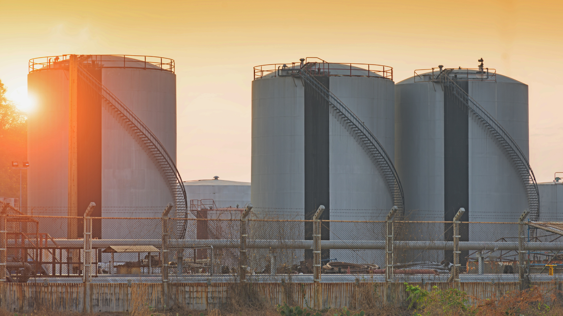 Sunlit industrial storage tanks with metal piping at a refinery at sunrise