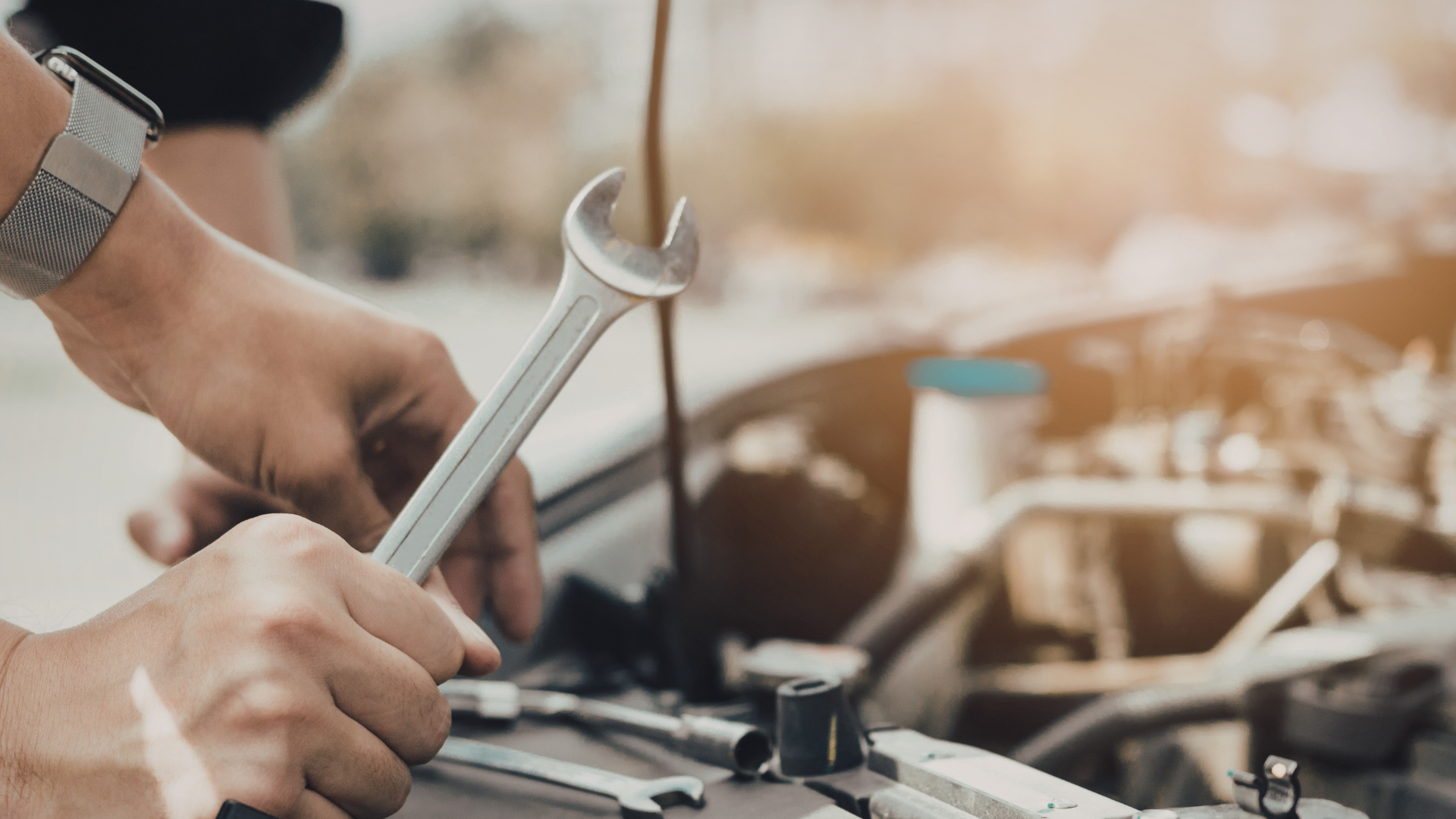 Hands using a wrench to repair a car engine in a garage