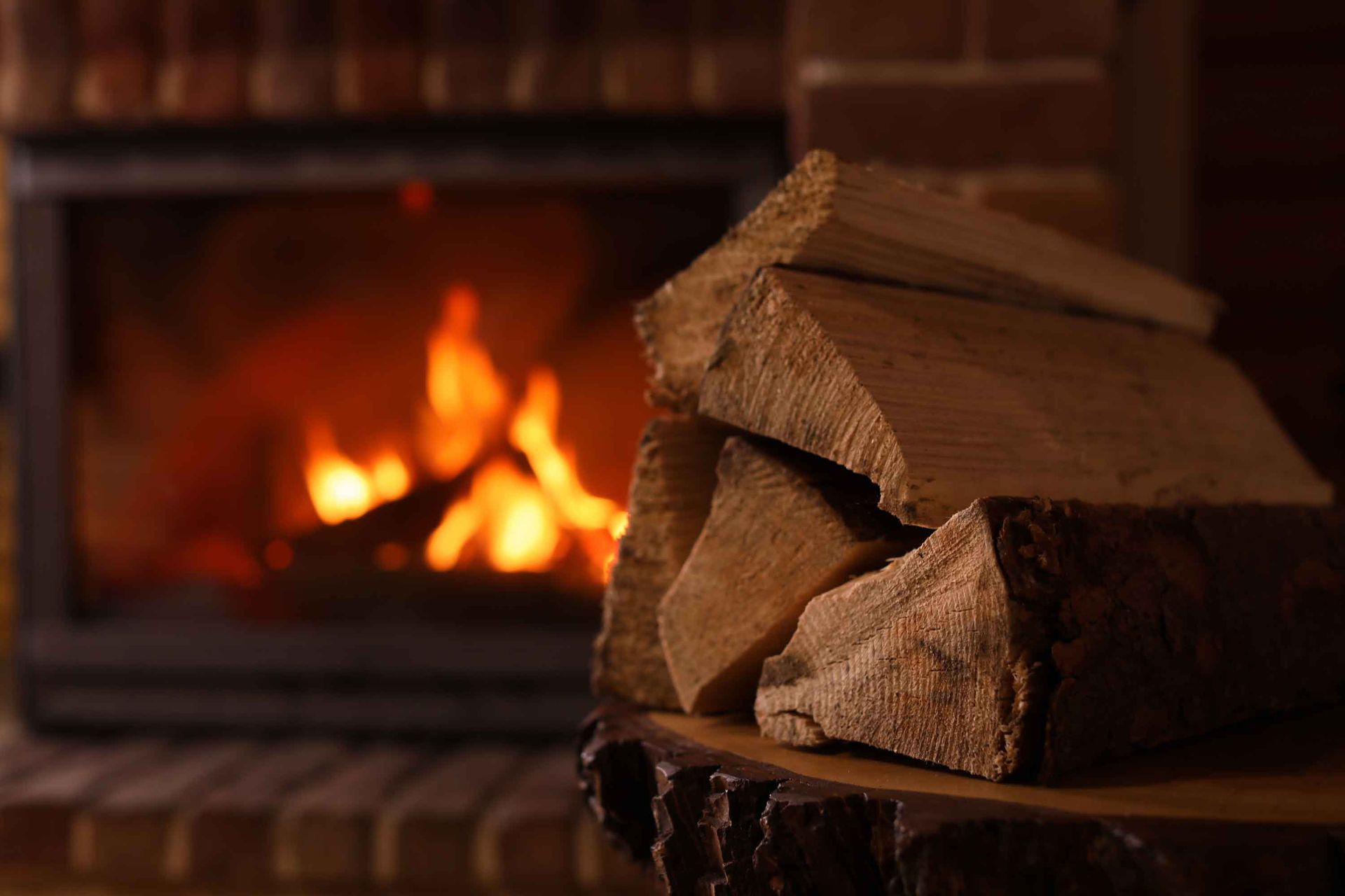 Close-up of a pile of wood, with a blurry and lit fireplace in the background. Close-up of a pile of wood, with a blurry and lit fireplace in the background.