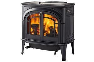 Black cast iron wood-burning stove with flames visible through glass doors. Black cast-iron wood stove with arched glass doors showing a bright orange fire inside