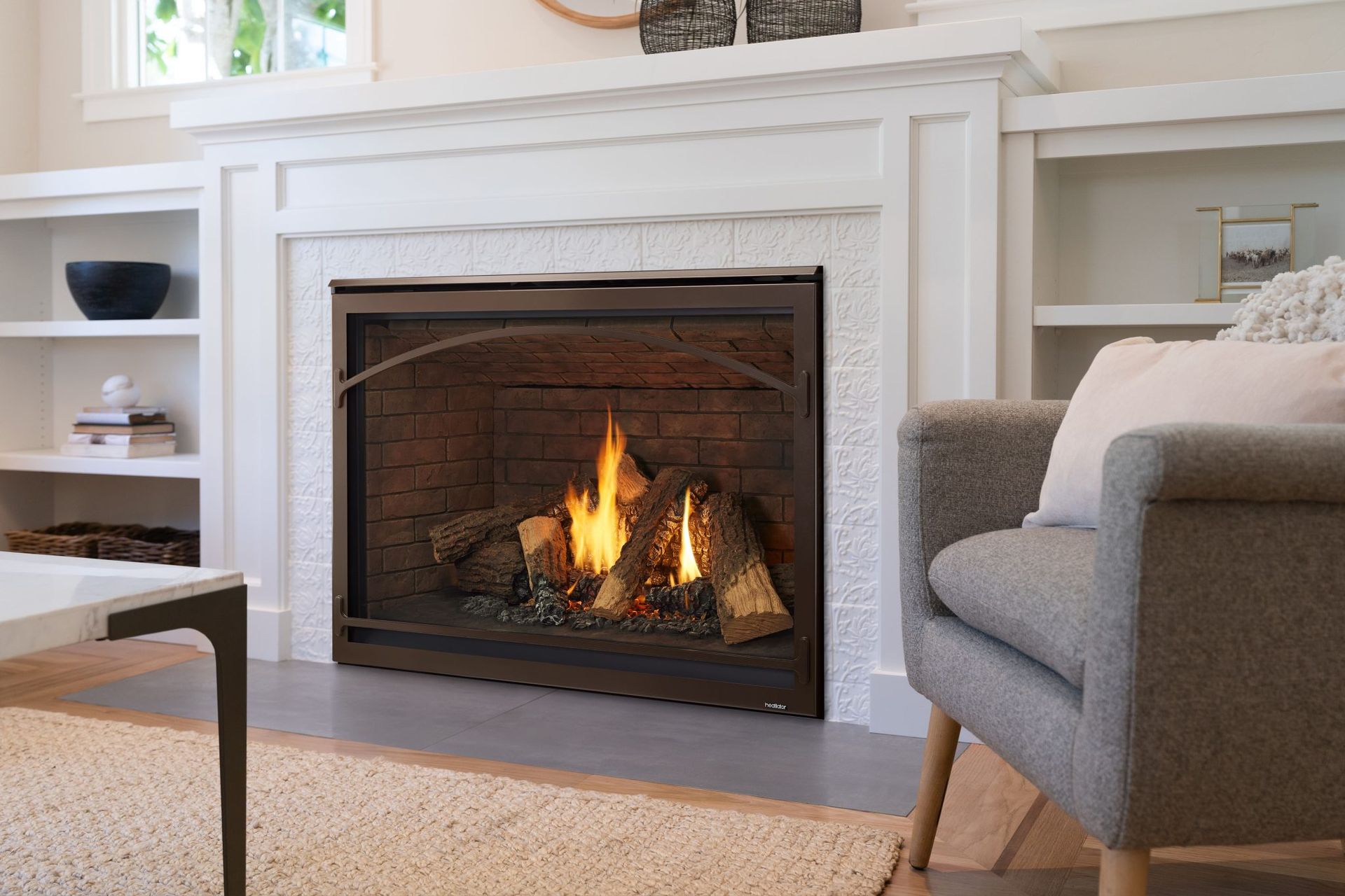 Fireplace with burning logs, flanked by white built-in shelves. Gray armchair. Fireplace with burning logs, flanked by white built-in shelves. Gray armchair.