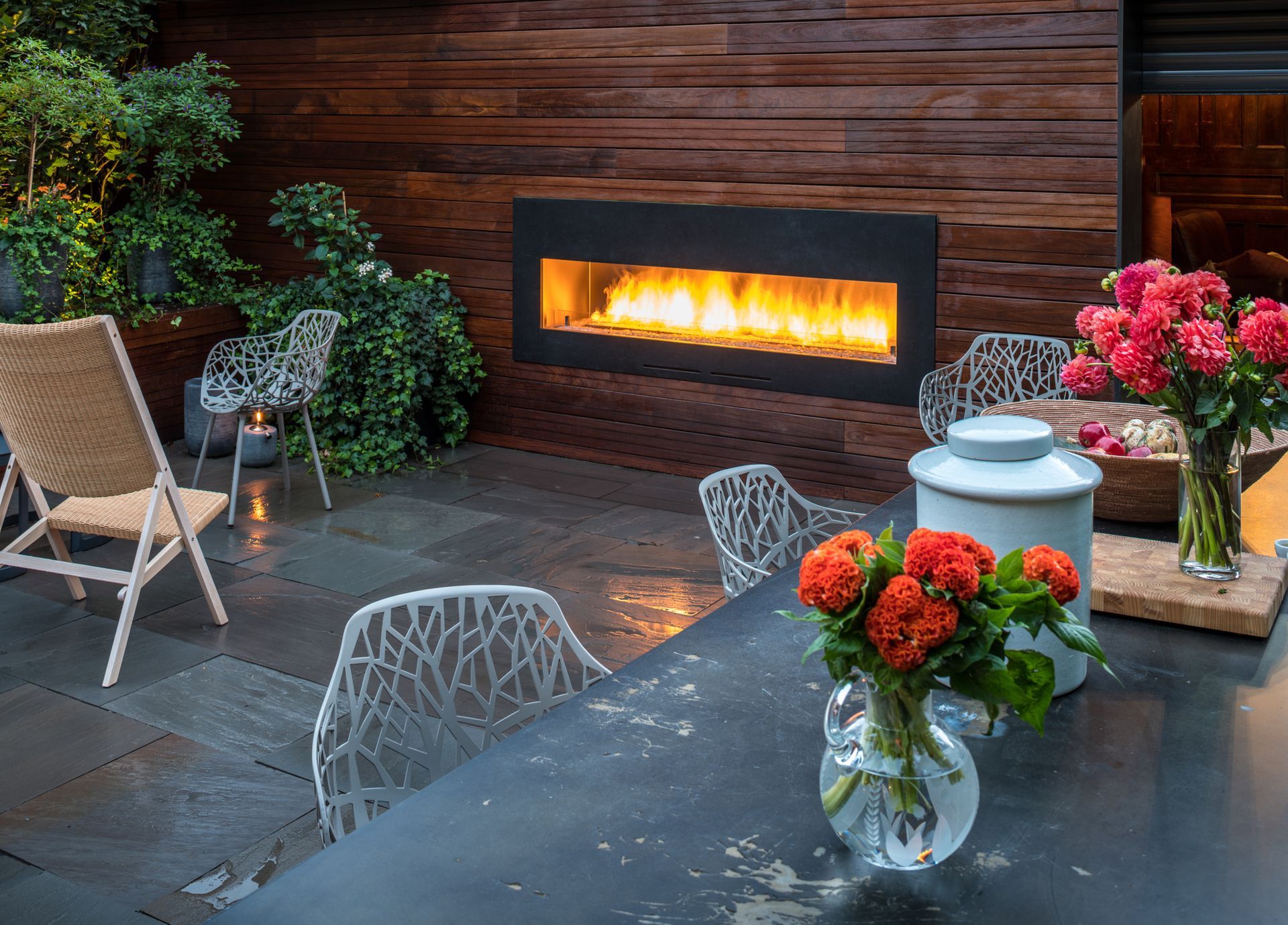 Outdoor patio with fireplace, seating, flowers, and wooden wall. Outdoor patio with fireplace, seating, flowers, and wooden wall.