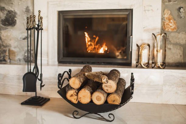 Fire burning in a white stone fireplace with a log basket in front and fireplace tools beside it
