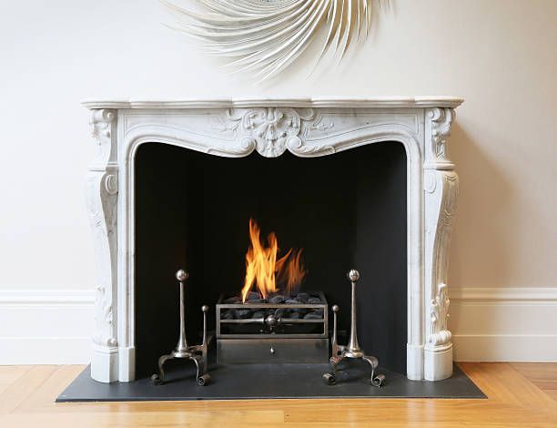 White ornate fireplace with a small fire burning inside on a hardwood floor