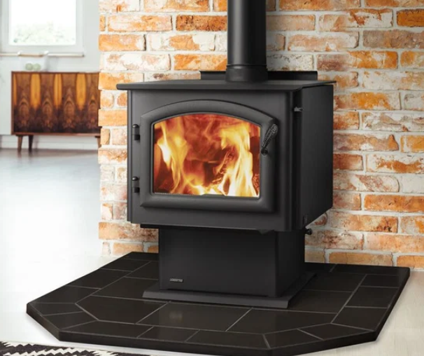 Quadra-Fire Millennium Series Black wood stove with visible fire on a tiled hearth in a brick-walled room