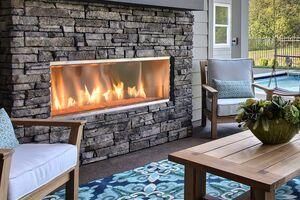 Outdoor fireplace with stone facade, flames, and seating area near a pool.
