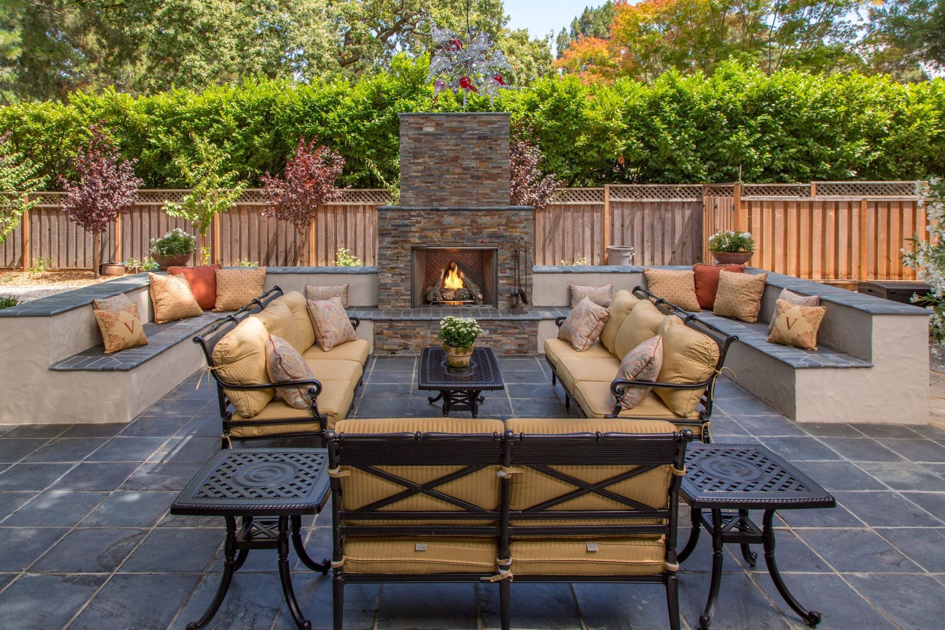 Outdoor patio with fireplace, seating areas, and a lush green hedge backdrop. Outdoor patio with fireplace, seating areas, and a lush green hedge backdrop.