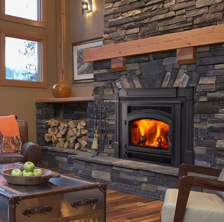 Quadra-Fire Expedition Cozy living room with a lit stone fireplace, stacked firewood, and warm wood accents