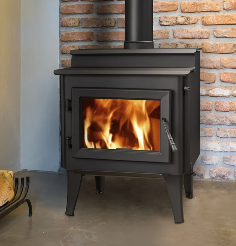 Quadra-Fire Step Top Series Black wood-burning stove with a fire burning inside, set against a brick wall.