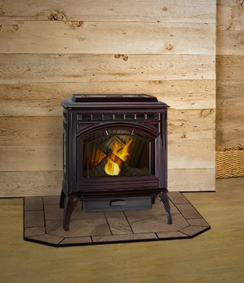 Quadra-Fire Trekker Black cast-iron wood stove with a fire burning, centered on a tiled hearth against a wood wall.