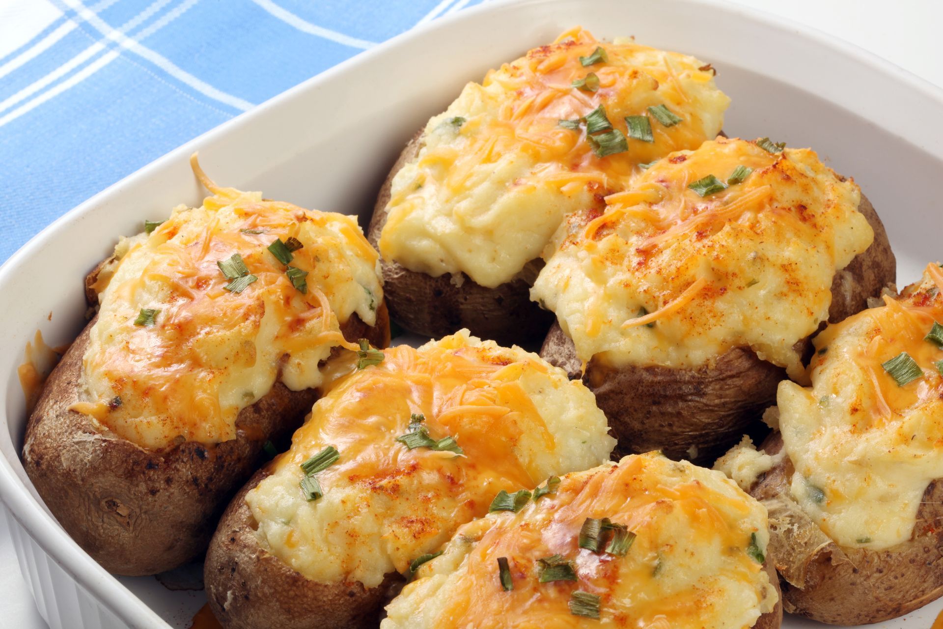 Stuffed baked potatoes topped with melted cheese and herbs in a white baking dish