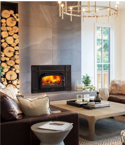Vermont Castings Montpelier II Modern living room with a lit fireplace, stacked firewood, beige sofa, and coffee table by a window