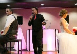 DJ at a wedding between bride and groom, in front of a light-up backdrop.